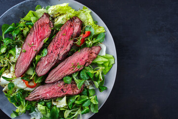 Traditional barbecue bavette beef steak slices with lambs salad and iceberg lettuce served as top...