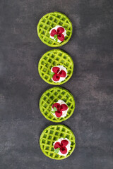 Green waffles. Round spinach soft waffles with cream cheese and raspberries. Dark gray background. Top view