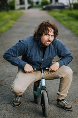 Obraz premium An adult underdeveloped crazy man, an idiot, an imbecile rides a children's small bicycle in a park on the road. Photography, mental illness, close-up portrait.