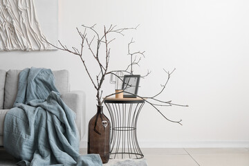 Interior of cozy living room with grey sofa tree branches in vase near white wall
