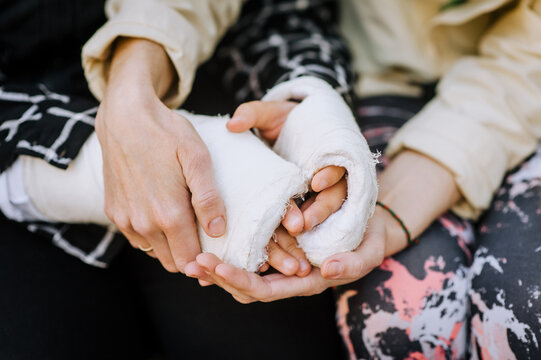 A caring woman, mother, girlfriend holds hands in a cast, bandage an injured sick girl, a child after a bone fracture, takes care, reassuring. Close-up photography, portrait, rehabilitation.