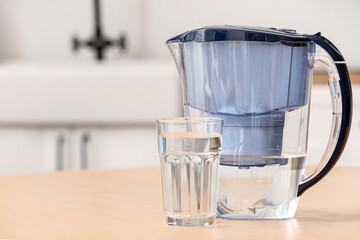 Glass of pure water and filter jug on wooden table in kitchen