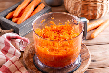 The grated carrots in an electric chopper on a table