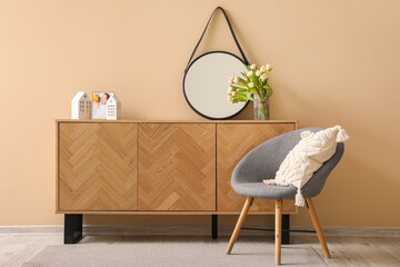 Armchair and wooden cabinet with stylish mirror near beige wall