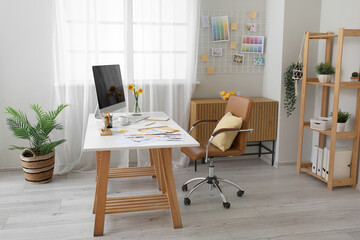 Comfortable designer's workplace with modern PC and beautiful narcissus flowers near window