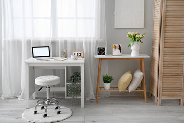 Comfortable workplace with modern laptop, cup of tea and beautiful tulip flowers near window
