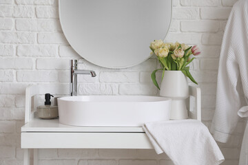 Mirror hanging on white brick wall near sink and vase with tulip flowers