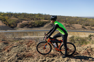Obraz premium Cyclist riding bicycle on offroad against clear sky. A man in an outfit stands with a bicycle on an autumn sunny day.