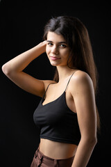 Classic studio portrait of a young brunette dressed in a black top, who is sitting on a chair against a black background.
