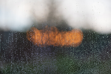 Rain drops on window glass on blurred forest background, blurred lights