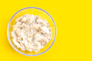 Mashed bananas in bowl on yellow background.