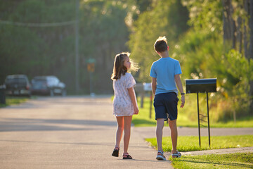 Two young teenage children, girl and boy standing and talking together outdoors on bright sunny day...