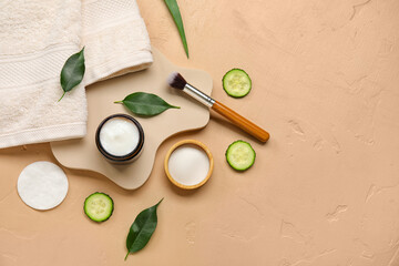 Composition with jar of natural cream, brush, cucumber and towel on color background