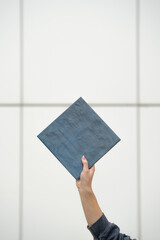Female Hand Holding Square Blue Tile Against White Tiled Background