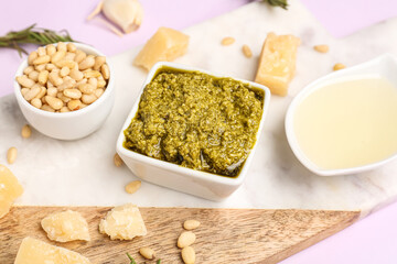 Bowl of delicious pesto sauce and ingredients on lilac background