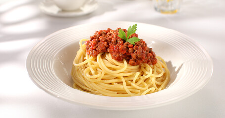 spaghetti bolognese on a white plate. classic italian pasta with meat tomato sauce on a white background. dish of mediterranean cuisine. food on the table on a sunny day. yellow noodles, minced meat.