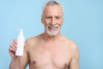 Handsome senior man showing at camera a white bottle with cosmetic beauty product, isolated on blue