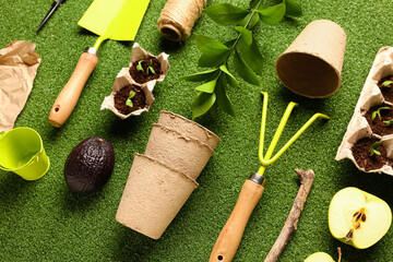 Cardboard boxes with seedlings, peat pots, fruits, and gardening tools on green background