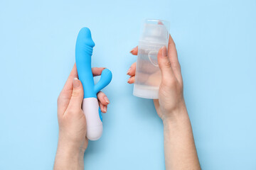 Woman holding vibrator and bottle of lubricant on blue background