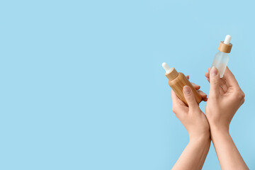 Hands holding bottles with cosmetic serum on light blue background