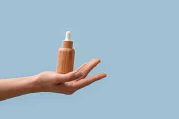 Hand holding bottle with cosmetic serum on light blue background