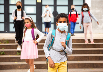 African american tween schoolboy in protective mask with backpacks going to school lessons on fall...