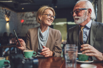 Stylish Senior Business Partners Sharing Digital Insights at Cafe