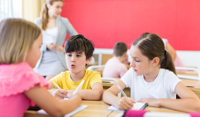 Schoolkids performing group tasks during lesson. Their teacher standing and observing.