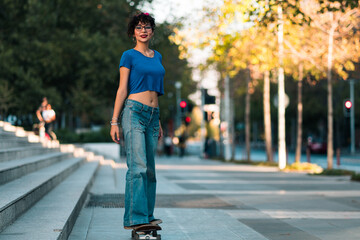 bella mujer adolescente estilo 80s 90s andando en skate en la ciudad, con maquillaje, anteojos y jeans. en un día soleado al atardecer.