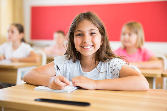 Smiling diligent elementary school student tween girl studying with classmates, making notes of teacher lecture