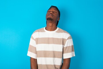 Handsome man wearing striped t-shirt and cap over blue background looking sleepy and tired, exhausted for fatigue and hangover, lazy eyes in the morning.