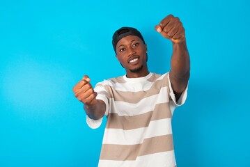 Handsome man wearing striped t-shirt and cap over blue background imagine steering wheel helm rudder passing driving exam good mood fast speed