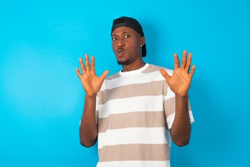 Handsome man wearing striped t-shirt and cap over blue background Moving away hands palms showing...