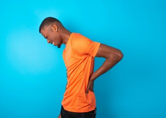 Handsome man wearing orange T-shirt over blue background Suffering of backache, touching back with hand, muscular pain