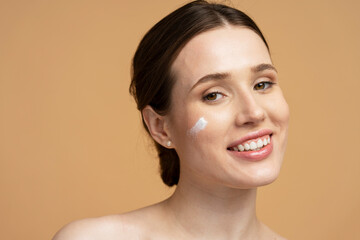 Closeup portrait of beautiful smiling young woman applying cream on face looking at camera