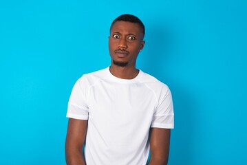 Displeased Handsome man wearing white T-shirt over blue background frowns face feels unhappy has some problems. Negative emotions and feelings concept