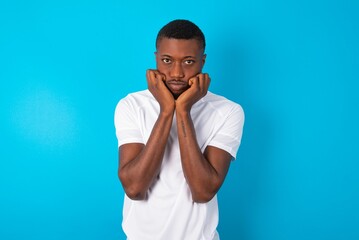 Portrait of sad Handsome man wearing white T-shirt over blue background hands face