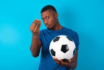 Young man wearing sport T-shirt holding a ball over blue background Doing Italian gesture with hand and fingers confident expression