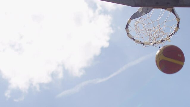 Closer shot of basketball sailing through the air in slow motion before passing through an outdoor net