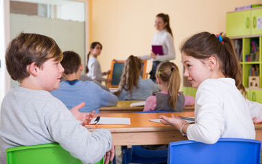 Fototapeta na wymiar Happy pupils chattering sitting on back desks at lesson in elementary school
