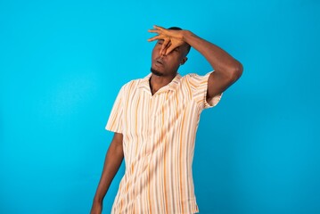 Displeased young man wearing fashion shirt over blue background plugs nose as smells something...