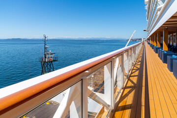 An outdoor deck with railing and seating on a cruise ship at sea, with the mountains of the Pacific...