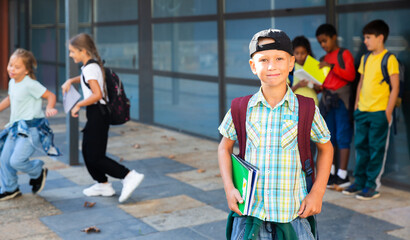 Smiling boy standing after classes near school with fellow classmates on background