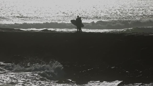 Couple of surfers standing on the rock by the sea