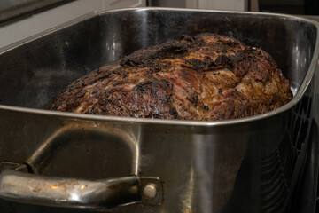 A large Angus beef prime rib roast cooked in a roaster pan with onions. The shiny metal pan is rectangular in shape with handles. The medium to well done roast is covered in garlic and spices.