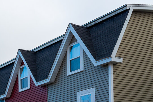 Two adjoined houses with peaked dormers over double hung windows with white trim. The mansard roof has black shingles. The exterior walls are red and tan colored wood siding. The duplex roof is flat.  - Powered by Adobe