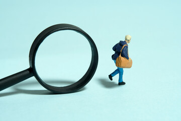 Miniature tiny people toy figure photography. A college student running in front of magnifier glass. Isolated on blue background