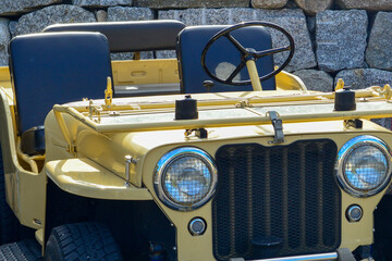 A vibrant yellow colored two-door civilian Jeep with the roof off. The antique auto has two black...