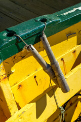 Downward view of a yellow wooden boat with dark green trim you can see a wood dildo and rope. The boat is tied up at the dock using a rope. The water looks almost green and transparent. 