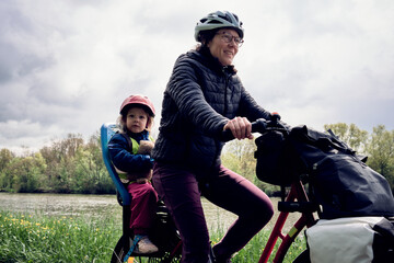 Exploration en vélo d'une jeune maman et fille le long du canal sous un ciel lumineux - obrazy, fototapety, plakaty